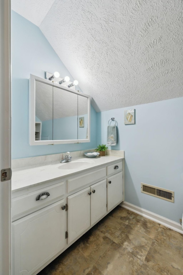 bathroom featuring visible vents, vaulted ceiling, a textured ceiling, vanity, and baseboards