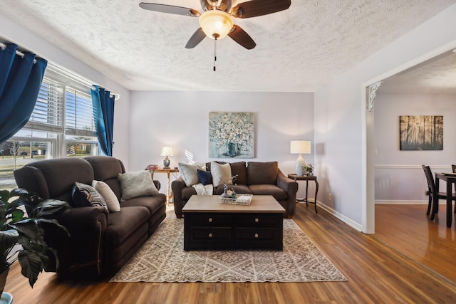 living area featuring a textured ceiling, wood finished floors, a ceiling fan, and baseboards