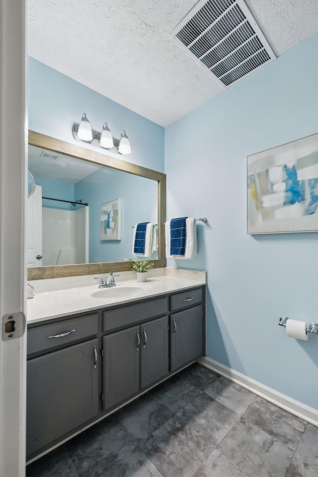 full bath featuring a textured ceiling, vanity, visible vents, baseboards, and a shower