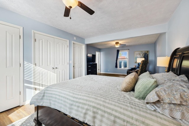 bedroom featuring a textured ceiling, wood finished floors, two closets, and a ceiling fan