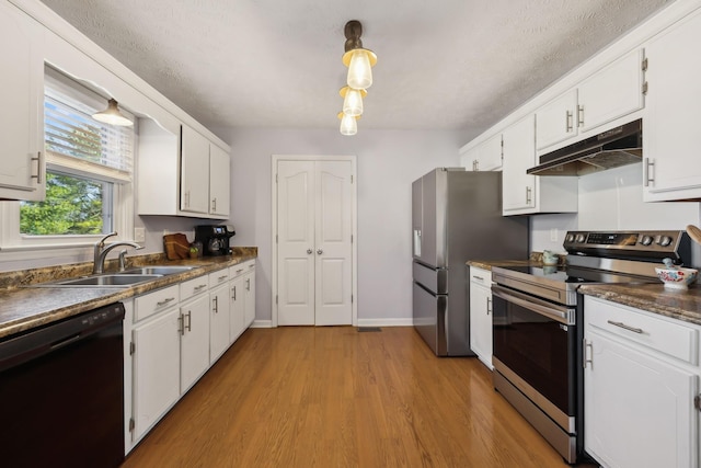 kitchen with dark countertops, appliances with stainless steel finishes, under cabinet range hood, white cabinetry, and a sink