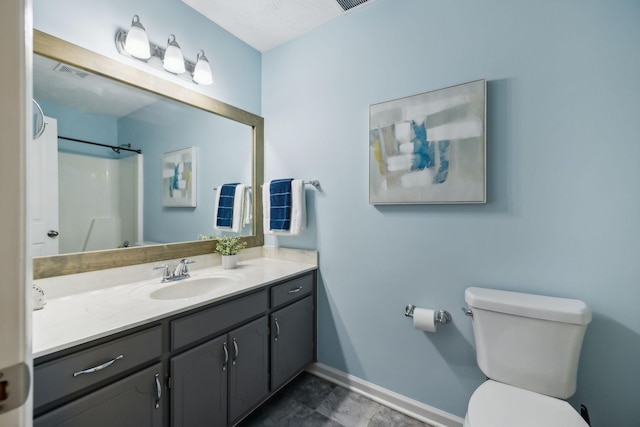 bathroom featuring toilet, vanity, visible vents, baseboards, and walk in shower