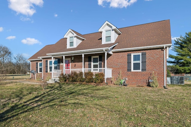 new england style home with a porch, a front lawn, a shingled roof, and brick siding