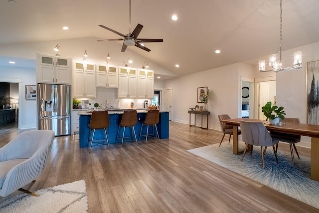 kitchen featuring a center island with sink, decorative backsplash, stainless steel fridge with ice dispenser, wood finished floors, and white cabinetry