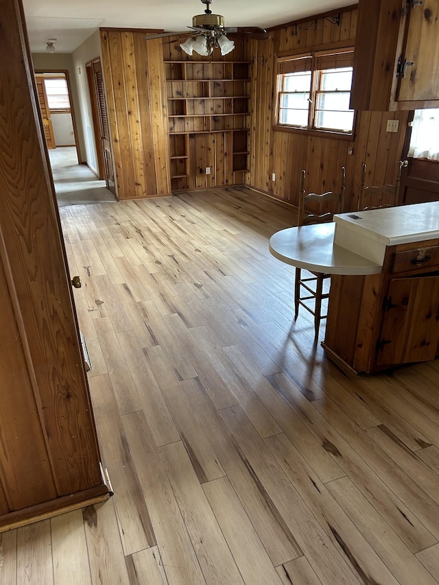 unfurnished dining area with light wood finished floors, ceiling fan, and wood walls