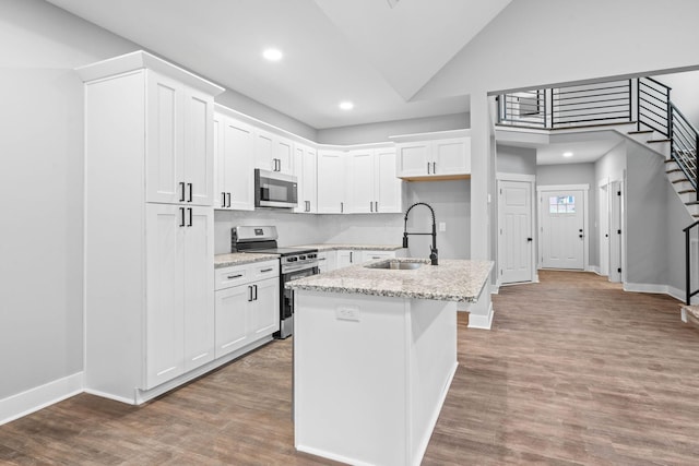 kitchen with stainless steel appliances, wood finished floors, white cabinets, a sink, and light stone countertops