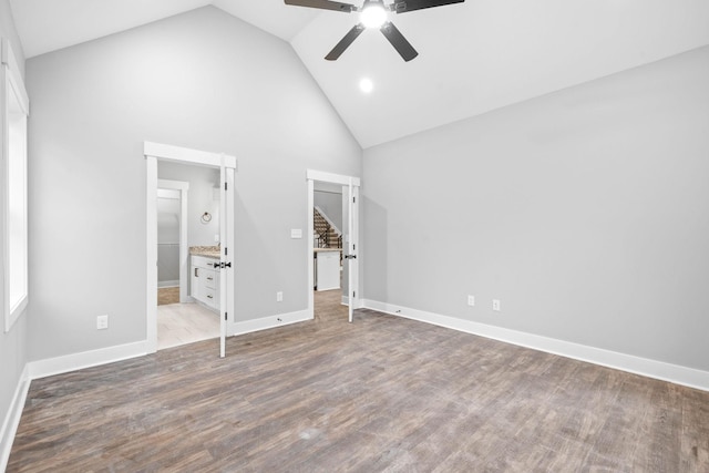 unfurnished bedroom featuring high vaulted ceiling, connected bathroom, wood finished floors, a ceiling fan, and baseboards