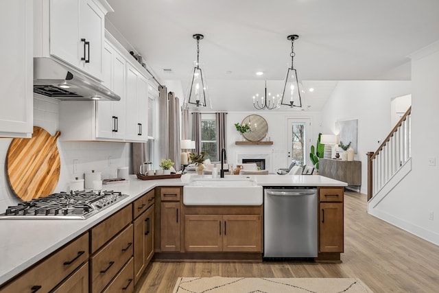 kitchen with appliances with stainless steel finishes, open floor plan, a peninsula, light countertops, and a sink