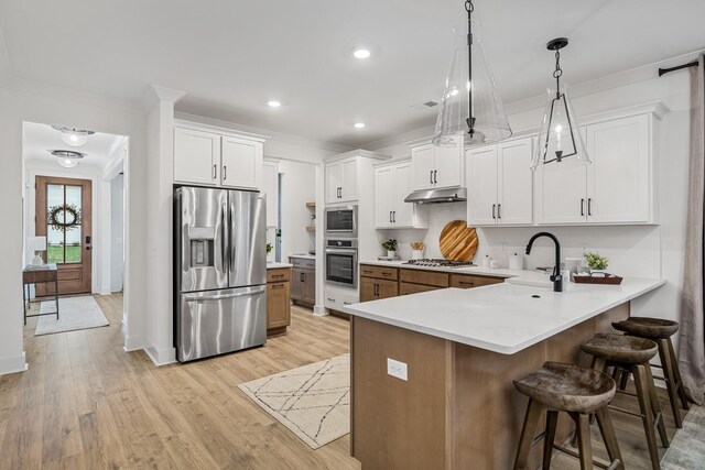 kitchen with appliances with stainless steel finishes, a peninsula, under cabinet range hood, a kitchen bar, and a sink