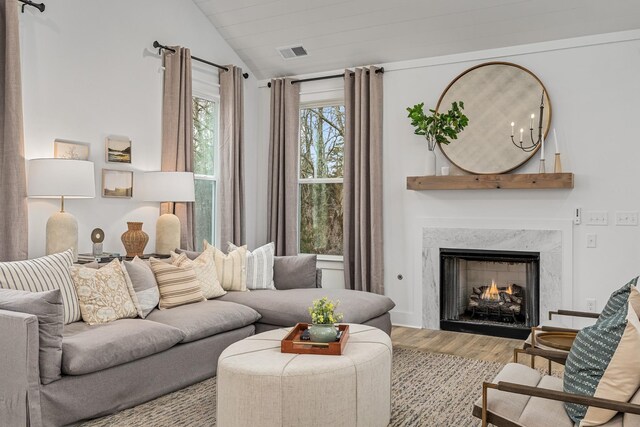 living room featuring lofted ceiling, a premium fireplace, visible vents, and wood finished floors