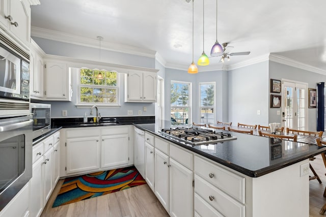 kitchen with dark countertops, appliances with stainless steel finishes, a sink, wood finished floors, and a peninsula