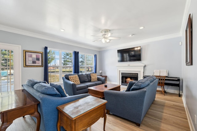 living room featuring light wood-style flooring, a ceiling fan, baseboards, a lit fireplace, and crown molding