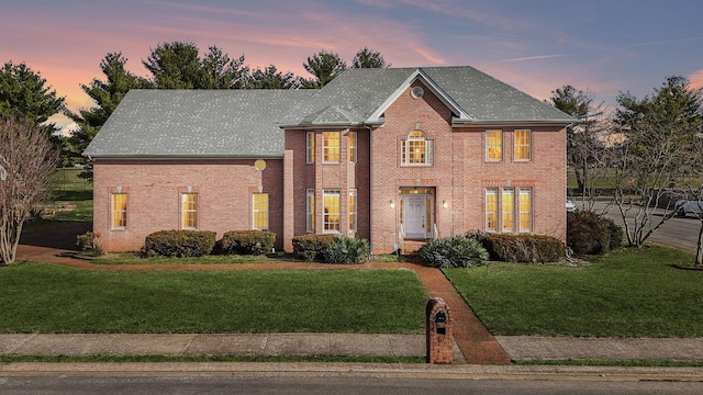 colonial house featuring a shingled roof, a lawn, and brick siding