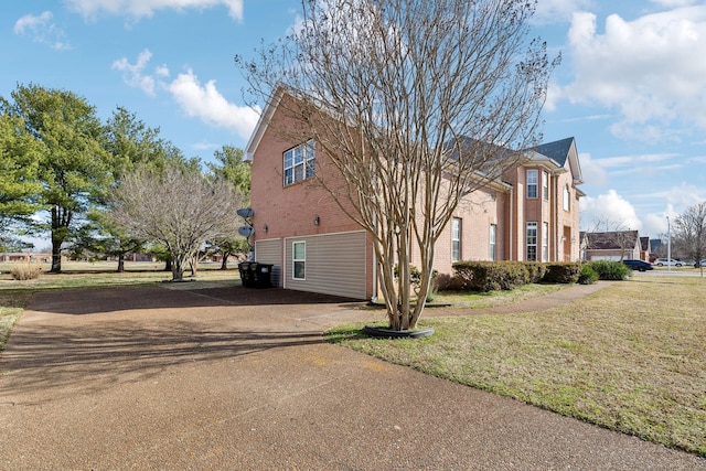 view of home's exterior with brick siding, aphalt driveway, and a yard