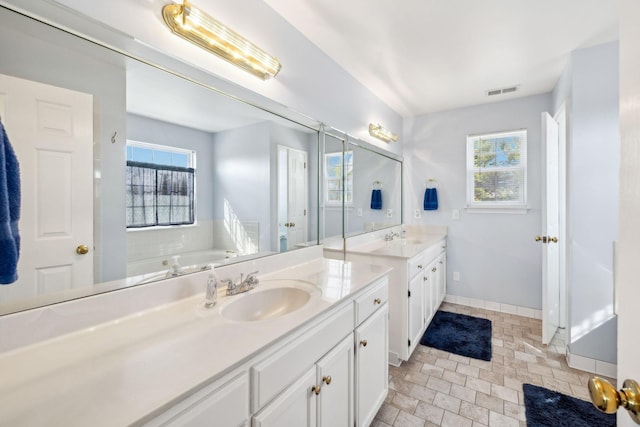 bathroom featuring visible vents, vanity, baseboards, and a bath