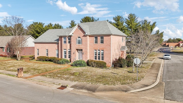 colonial-style house featuring roof with shingles, a front yard, and brick siding