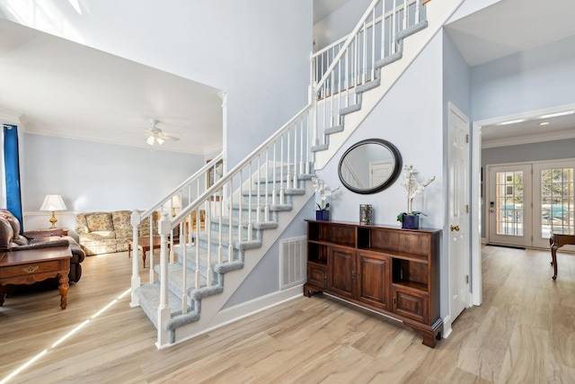 stairway with a towering ceiling, visible vents, ornamental molding, and wood finished floors