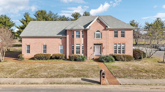 view of front of home featuring brick siding, roof with shingles, and a front yard