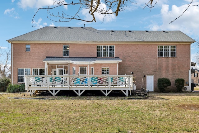 rear view of property featuring a shingled roof, a deck, a lawn, and brick siding