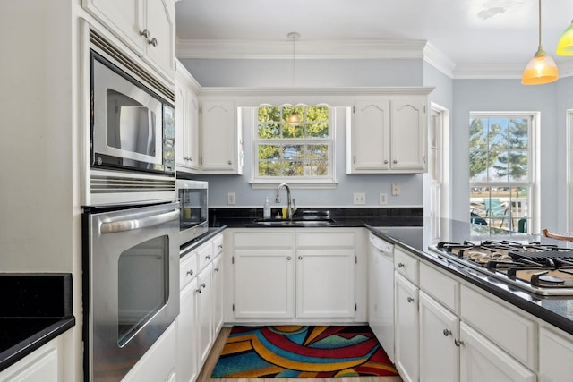 kitchen with dark countertops, appliances with stainless steel finishes, crown molding, white cabinetry, and a sink