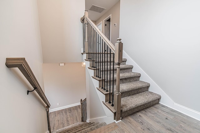 staircase with baseboards, visible vents, and wood finished floors