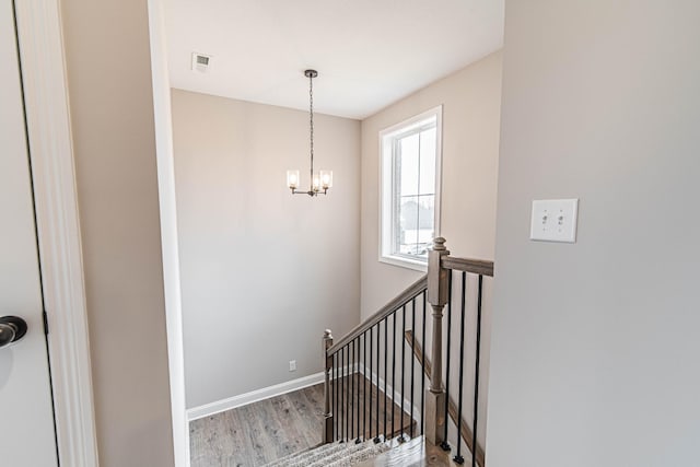 stairway with an inviting chandelier, visible vents, baseboards, and wood finished floors