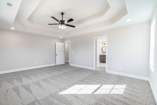 unfurnished bedroom featuring carpet floors, a tray ceiling, visible vents, ensuite bath, and baseboards