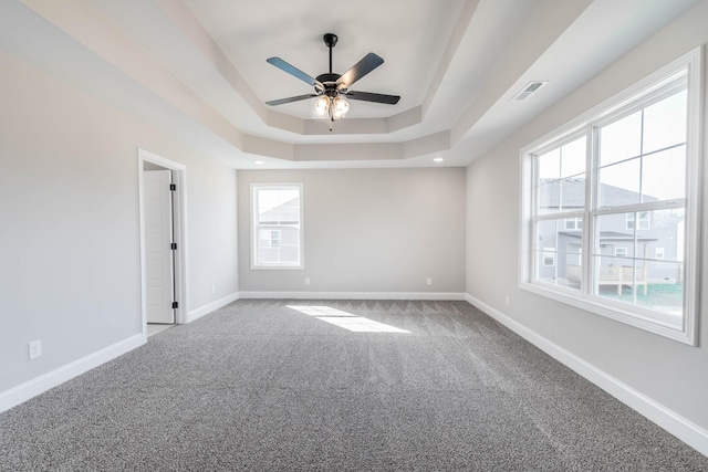 carpeted empty room featuring ceiling fan, a raised ceiling, visible vents, and baseboards