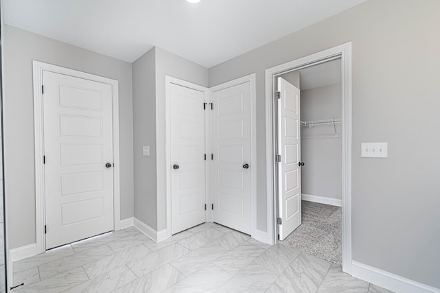 unfurnished bedroom with a closet, a walk in closet, marble finish floor, and baseboards