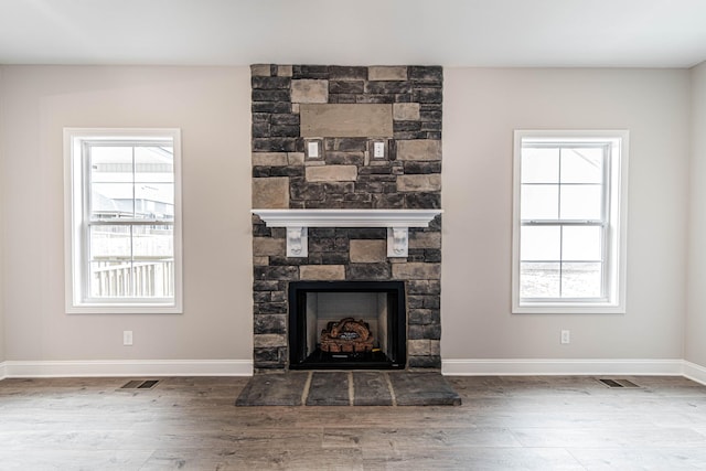 details featuring visible vents, baseboards, wood finished floors, and a stone fireplace