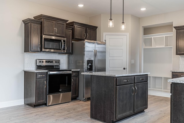 kitchen with stainless steel appliances, hanging light fixtures, light wood-type flooring, and light stone countertops