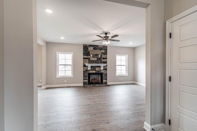 unfurnished living room with a healthy amount of sunlight, dark wood-style floors, baseboards, and a stone fireplace