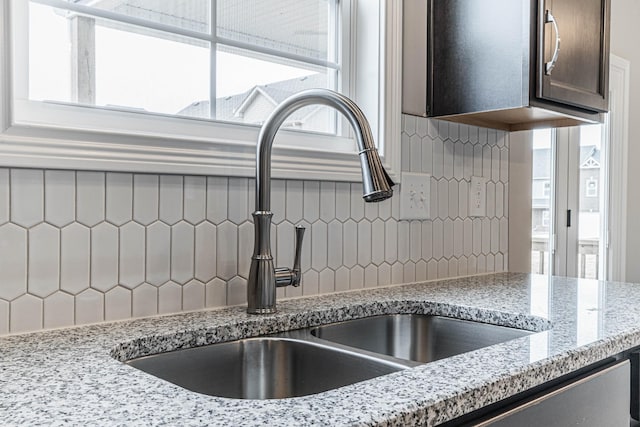 interior details featuring dark brown cabinets, backsplash, a sink, and light stone countertops