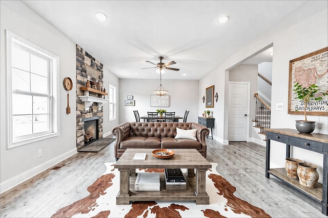 living area featuring light wood-style floors, recessed lighting, stairway, and a stone fireplace