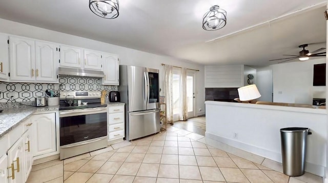 kitchen with light tile patterned floors, under cabinet range hood, stainless steel appliances, white cabinets, and decorative backsplash