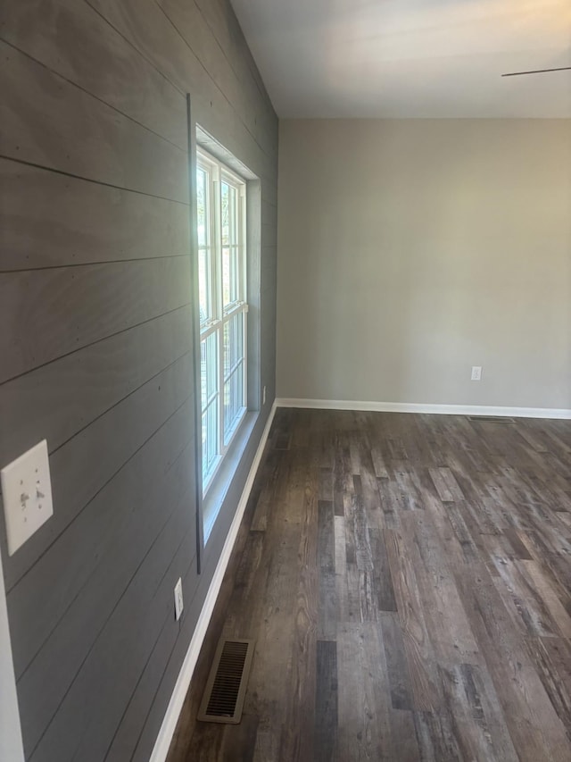 unfurnished room with dark wood-style flooring, visible vents, and baseboards