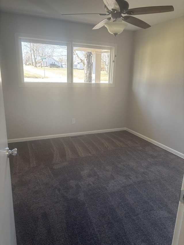 spare room featuring baseboards, dark carpet, and a ceiling fan