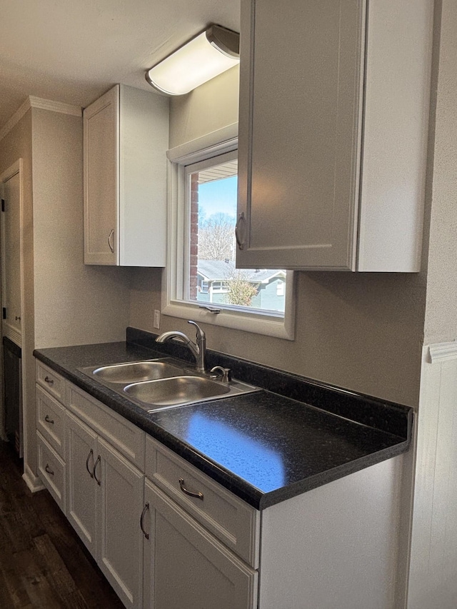 kitchen featuring dark wood-type flooring, dark countertops, a sink, and white cabinets