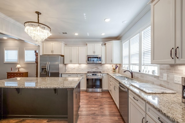 kitchen featuring crown molding, appliances with stainless steel finishes, a sink, a kitchen island, and a kitchen breakfast bar