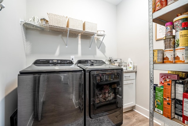 clothes washing area featuring washing machine and dryer, light wood-style flooring, and cabinet space