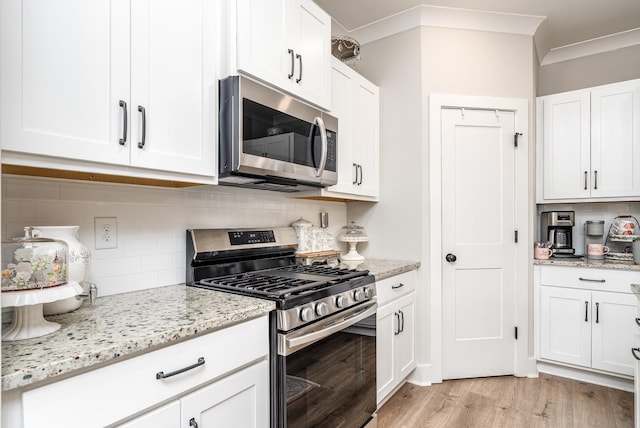 kitchen with light stone counters, tasteful backsplash, appliances with stainless steel finishes, light wood-type flooring, and white cabinets