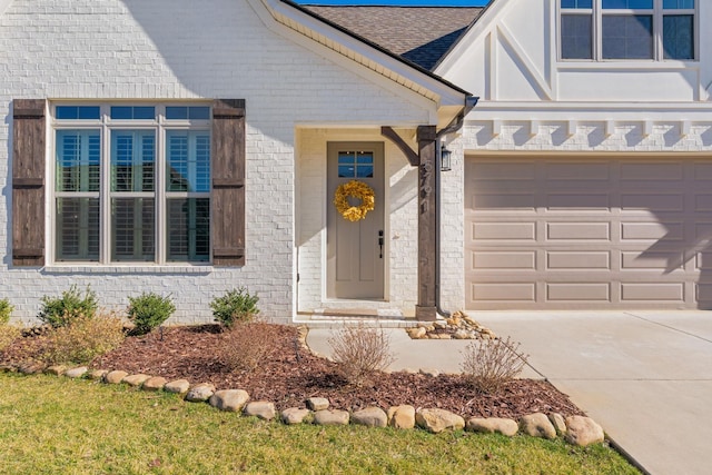 property entrance with an attached garage, brick siding, concrete driveway, and roof with shingles