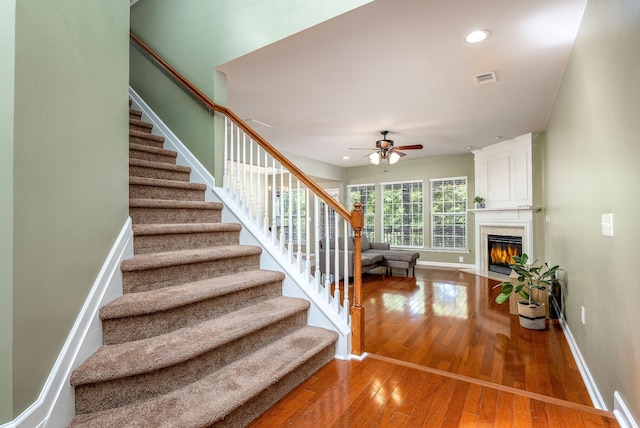 staircase with recessed lighting, visible vents, baseboards, a large fireplace, and hardwood / wood-style floors