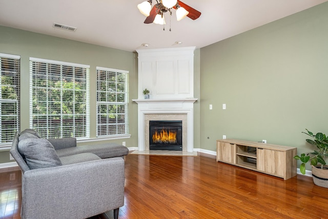 living area featuring baseboards, visible vents, a ceiling fan, wood finished floors, and a high end fireplace