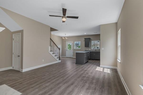 unfurnished living room with stairway, dark wood-style flooring, a sink, and baseboards