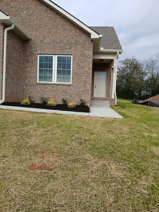 view of exterior entry with a yard, brick siding, and roof with shingles