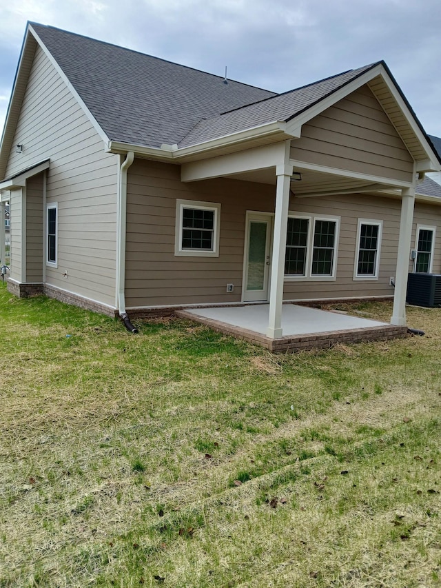 rear view of house with a yard, roof with shingles, a patio, and central air condition unit