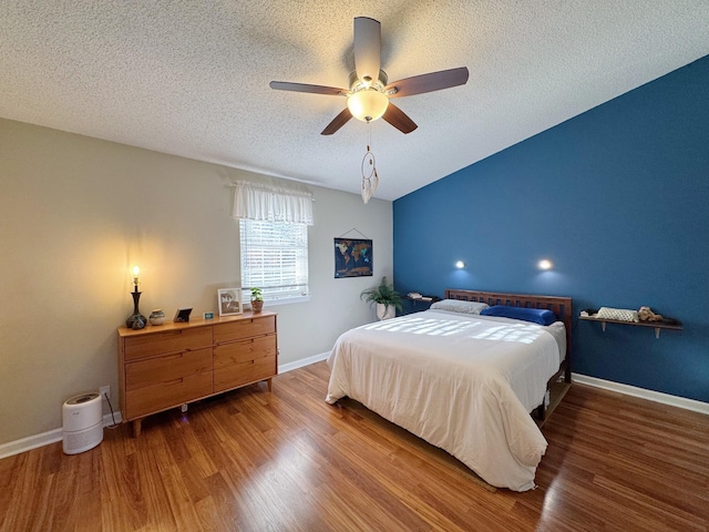 bedroom with a ceiling fan, a textured ceiling, baseboards, and wood finished floors