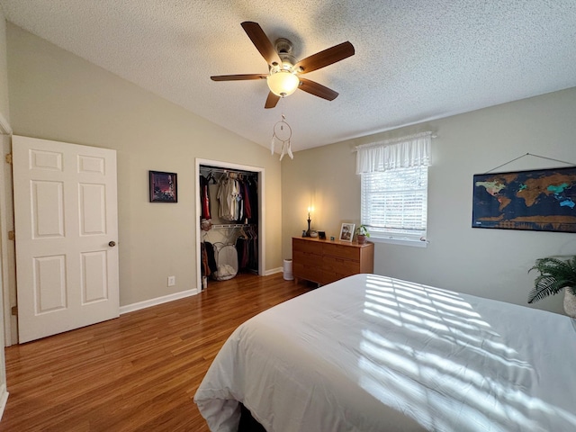 bedroom with lofted ceiling, ceiling fan, a textured ceiling, wood finished floors, and a closet