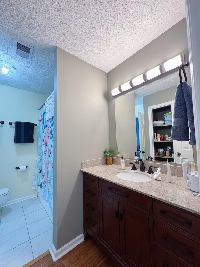 bathroom featuring a textured ceiling, toilet, vanity, visible vents, and baseboards